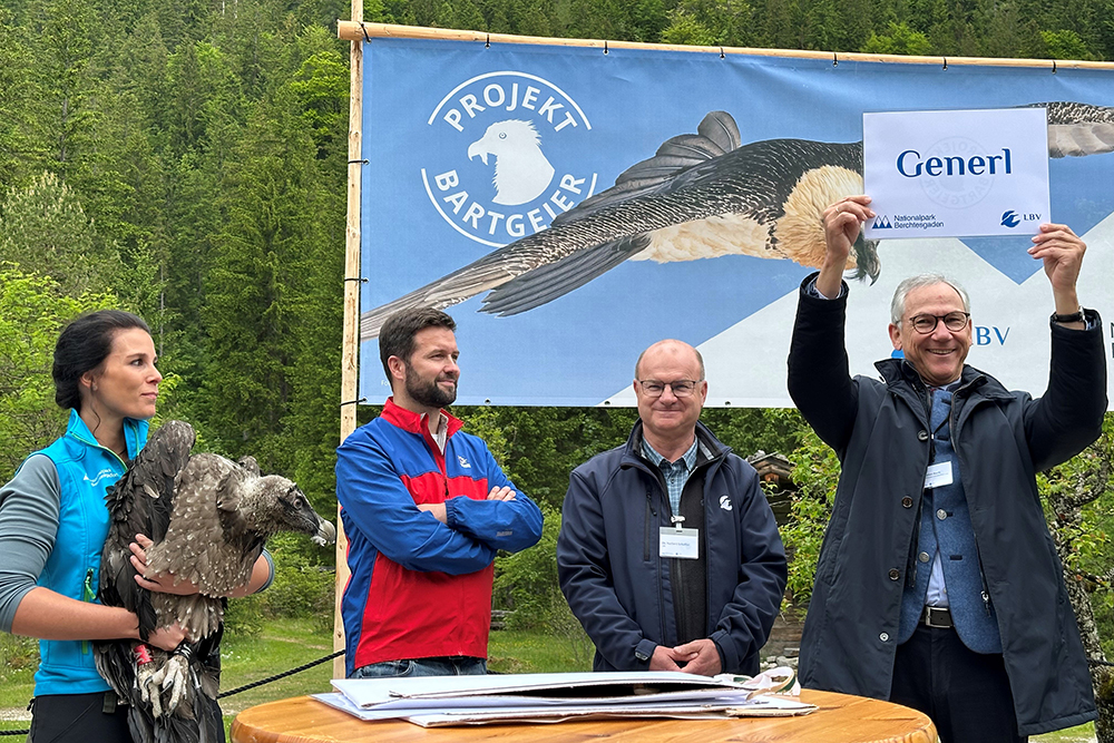 Dr. Christian Barth (l.) verlas die Namen der jungen Bartgeier. Hier Generl, gehalten von Nationalpark-Mitarbeiterin Magdalena Deelmann. Außerdem im Bild: Michael Renner, Leiter Bergwachtbereitschaft Ramsau als Namenspate und LBV-Vorsitzender Norbert Schäffer. - © NPV BGD